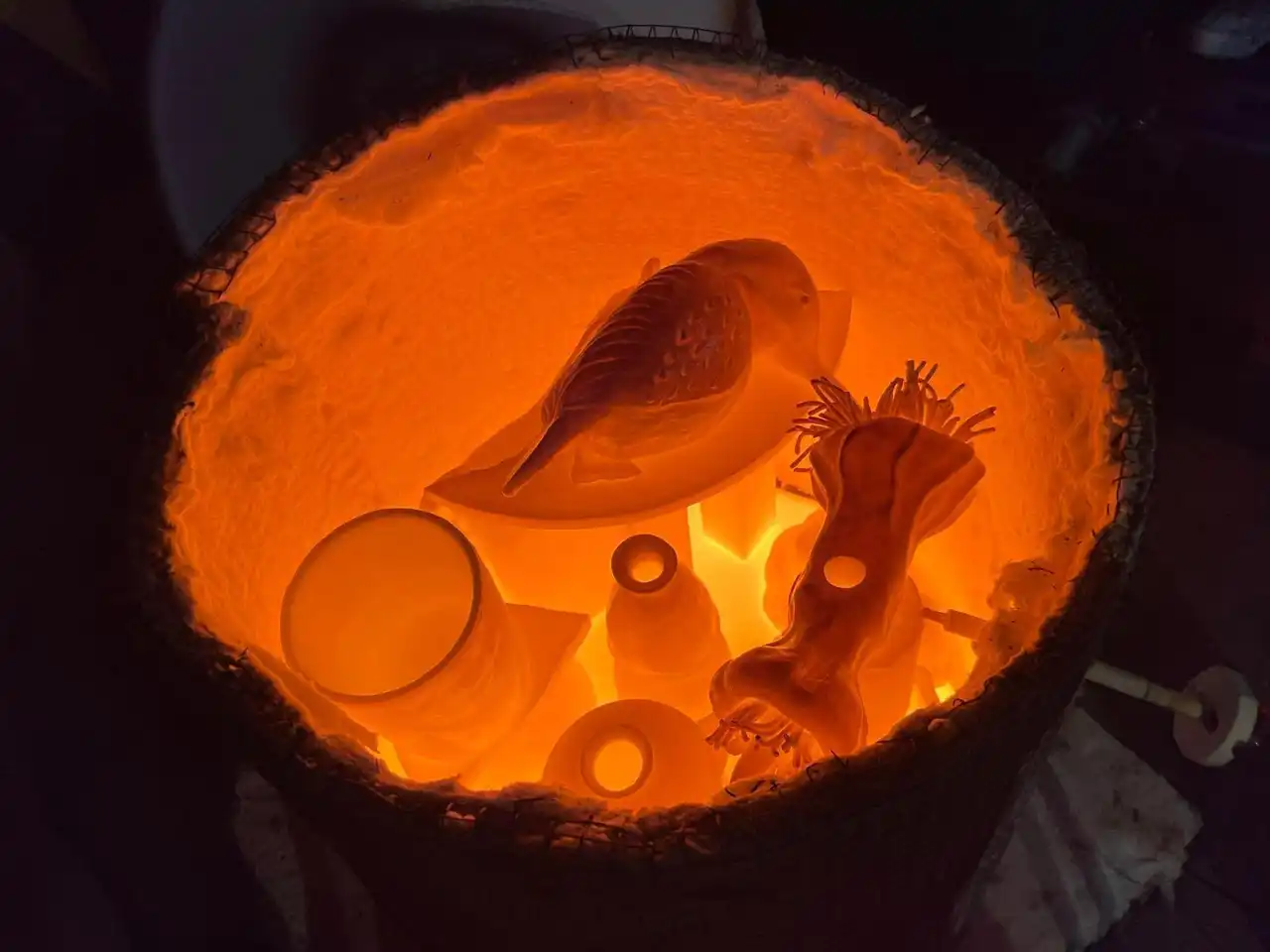 Looking into a raku kiln at full heat, with a ceramic bird and vessels glowing orange
